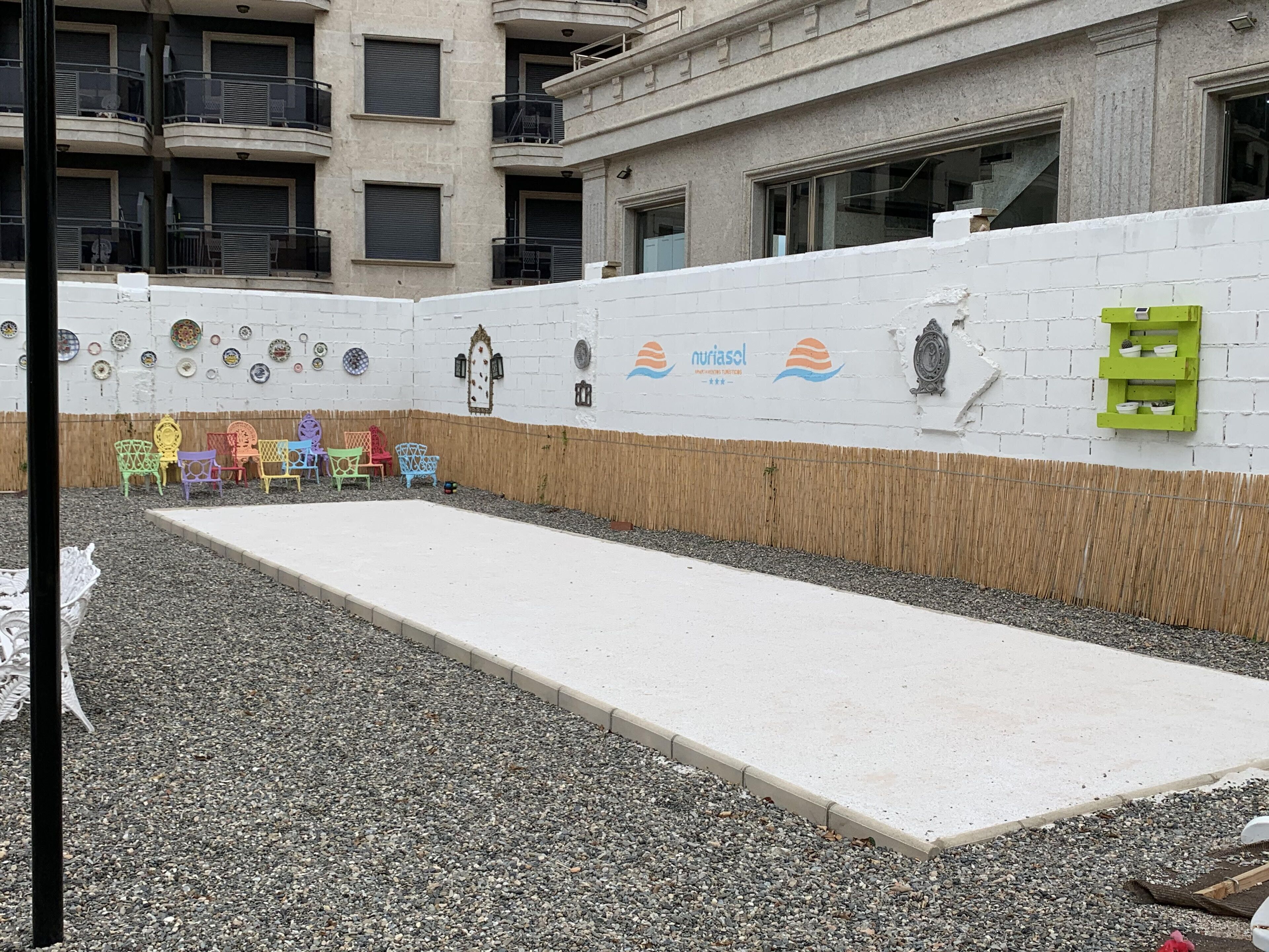 A building with a white exterior, a concrete ramp leading to a door, and colorful chairs lined up against the wall.