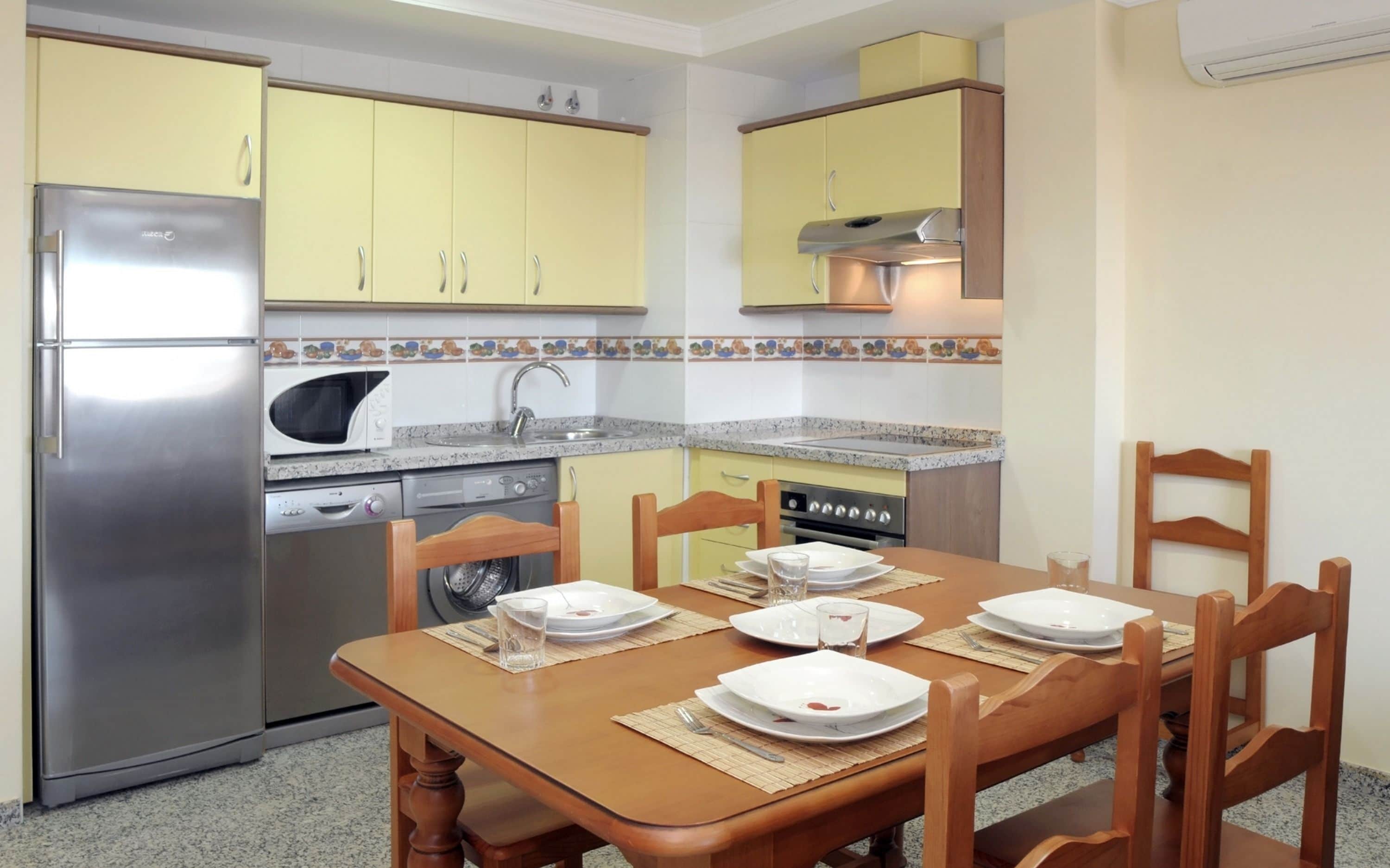 Une cuisine de taille réduite avec des meubles de couleur jaune, un réfrigérateur en acier inoxydable, un four à micro-ondes, une cuisinière et un lave-vaisselle.