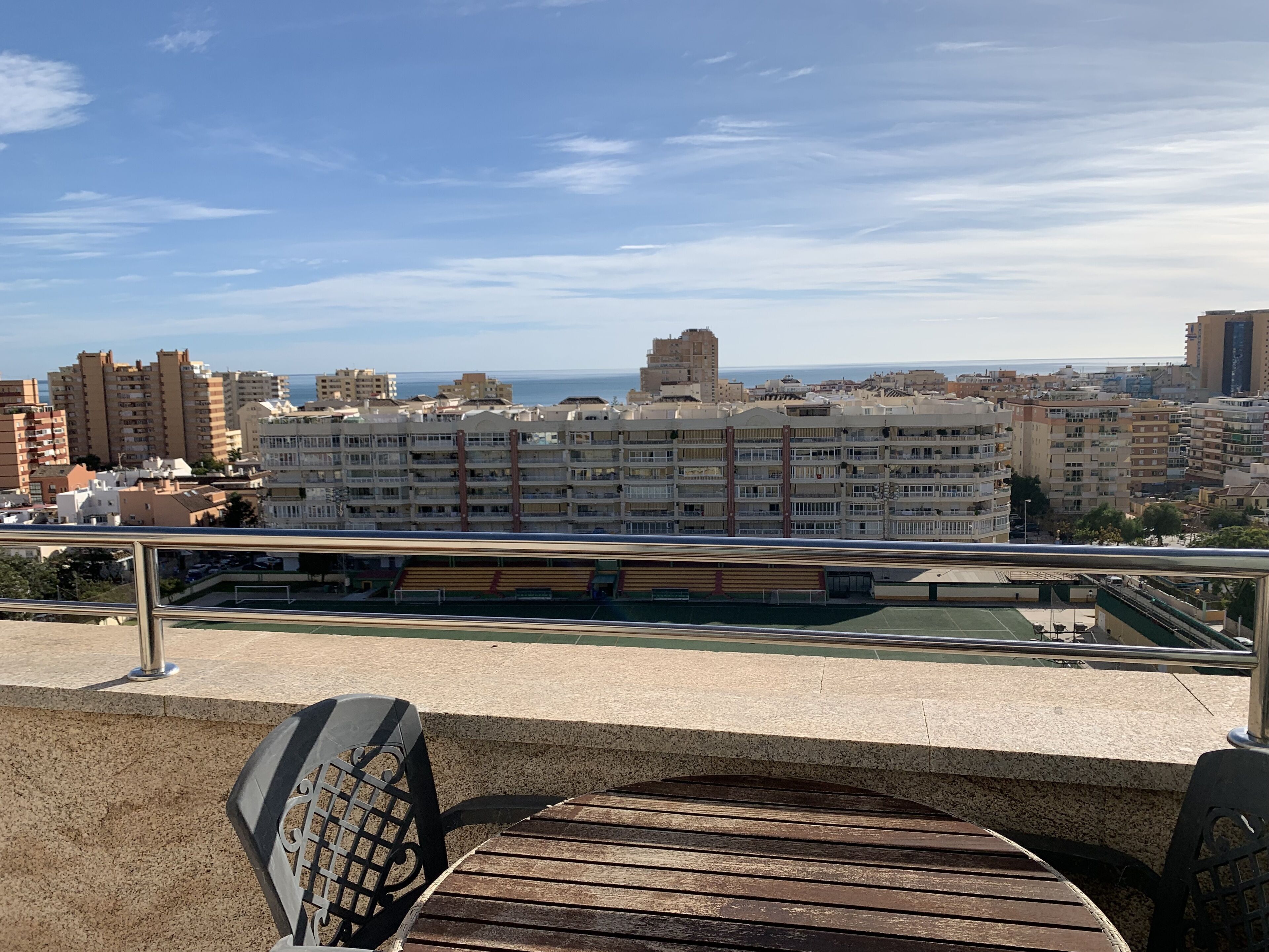 A rooftop terrace with a view of a coastal cityscape, featuring high-rise buildings and a clear sky.