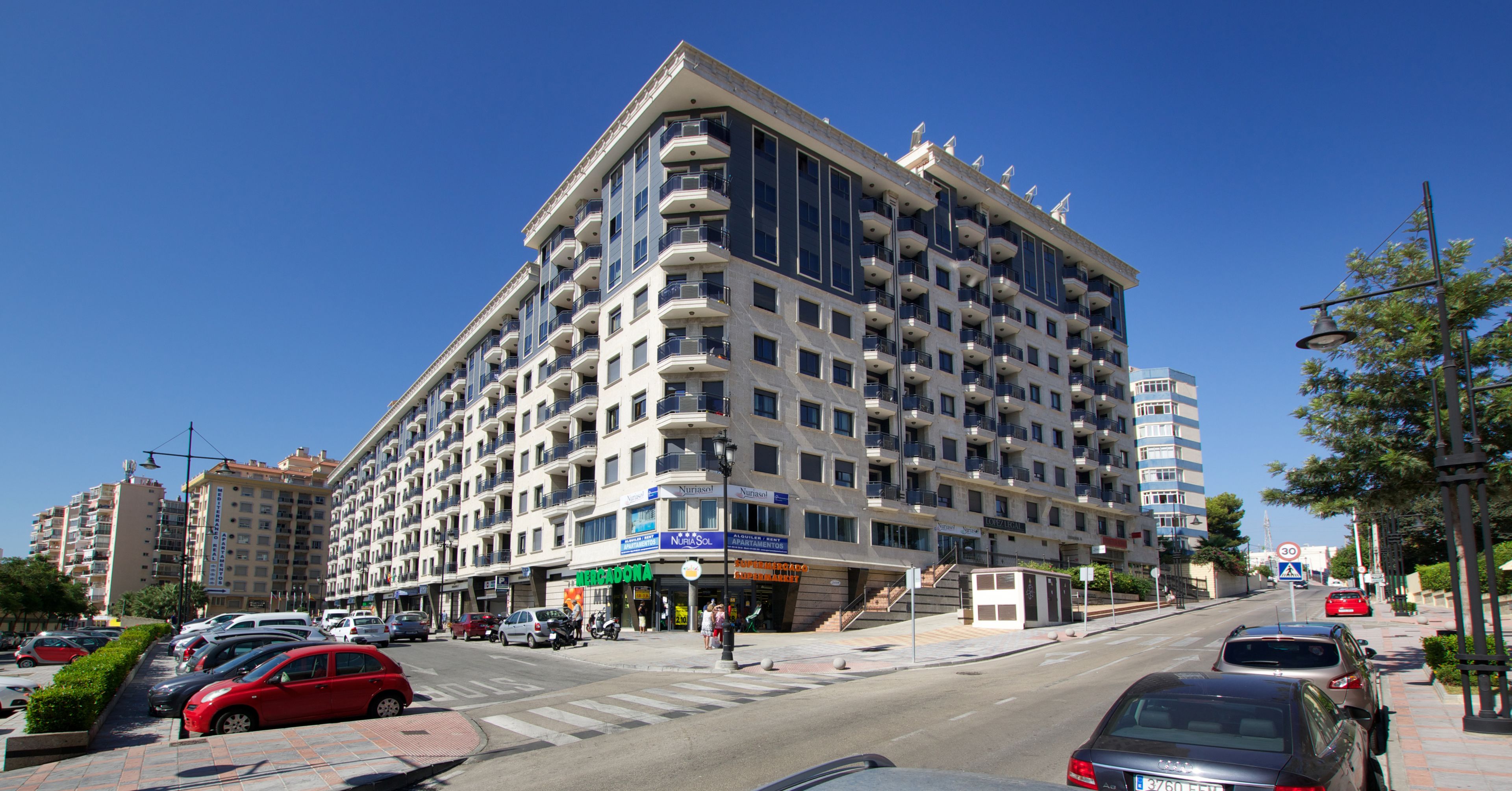 Un hotel de varios pisos con balcones, un restaurante en la planta baja y un paso de peatones.