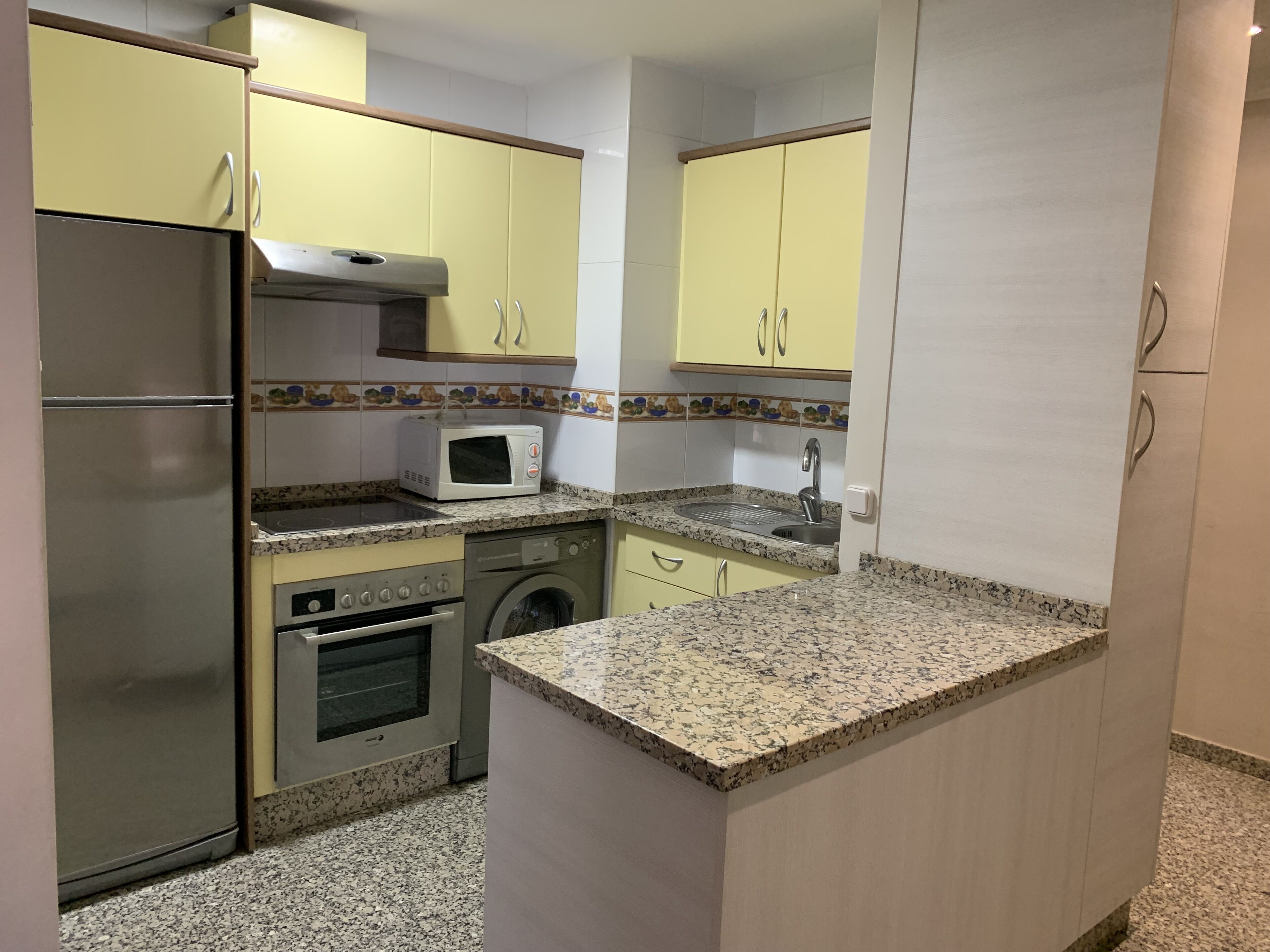 Eine kompakte Küche mit Edelstahl-Kühlschrank, Mikrowelle, Backofen und Waschmaschine.