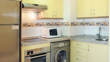 A compact kitchen with yellow cabinets, a stainless steel refrigerator, a microwave, an oven, and a washing machine.