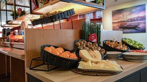A buffet counter with various food items, including fruits and cheeses, and a sign indicating a meat section. - ibis Porto Centro São Bento (Porto)