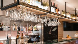 A bar area with a glass wine rack, shelves of liquor bottles, and a chalkboard menu. - ibis Porto Centro São Bento (Porto)