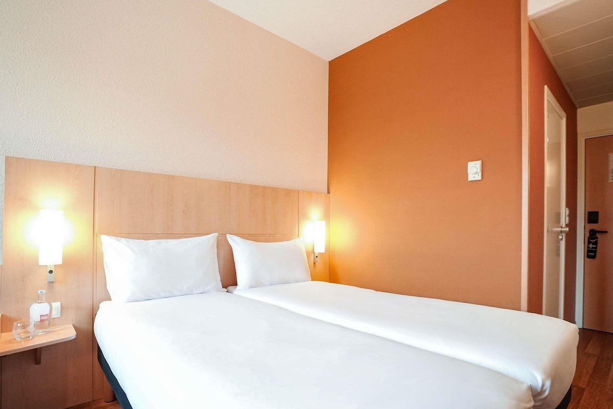 Ein Hotelzimmer mit einem großen Bett, zwei Nachttischen mit Lampen, einem hölzernen Kopfteil und einer orangenen Akzentwand.