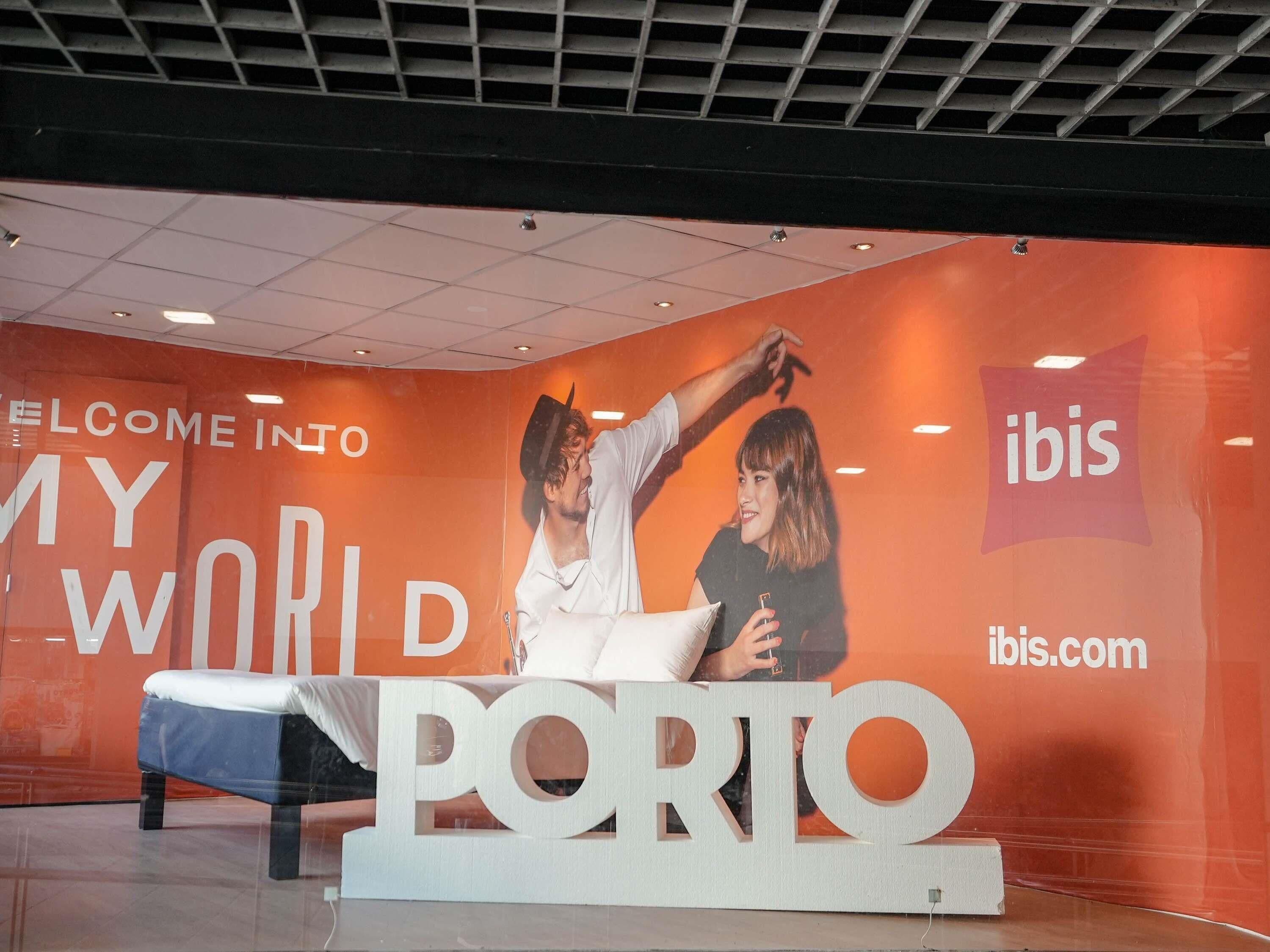 A promotional display with the text "WELCOME INTO MY WORLD PORTO" and "ibis.com" against an orange background.