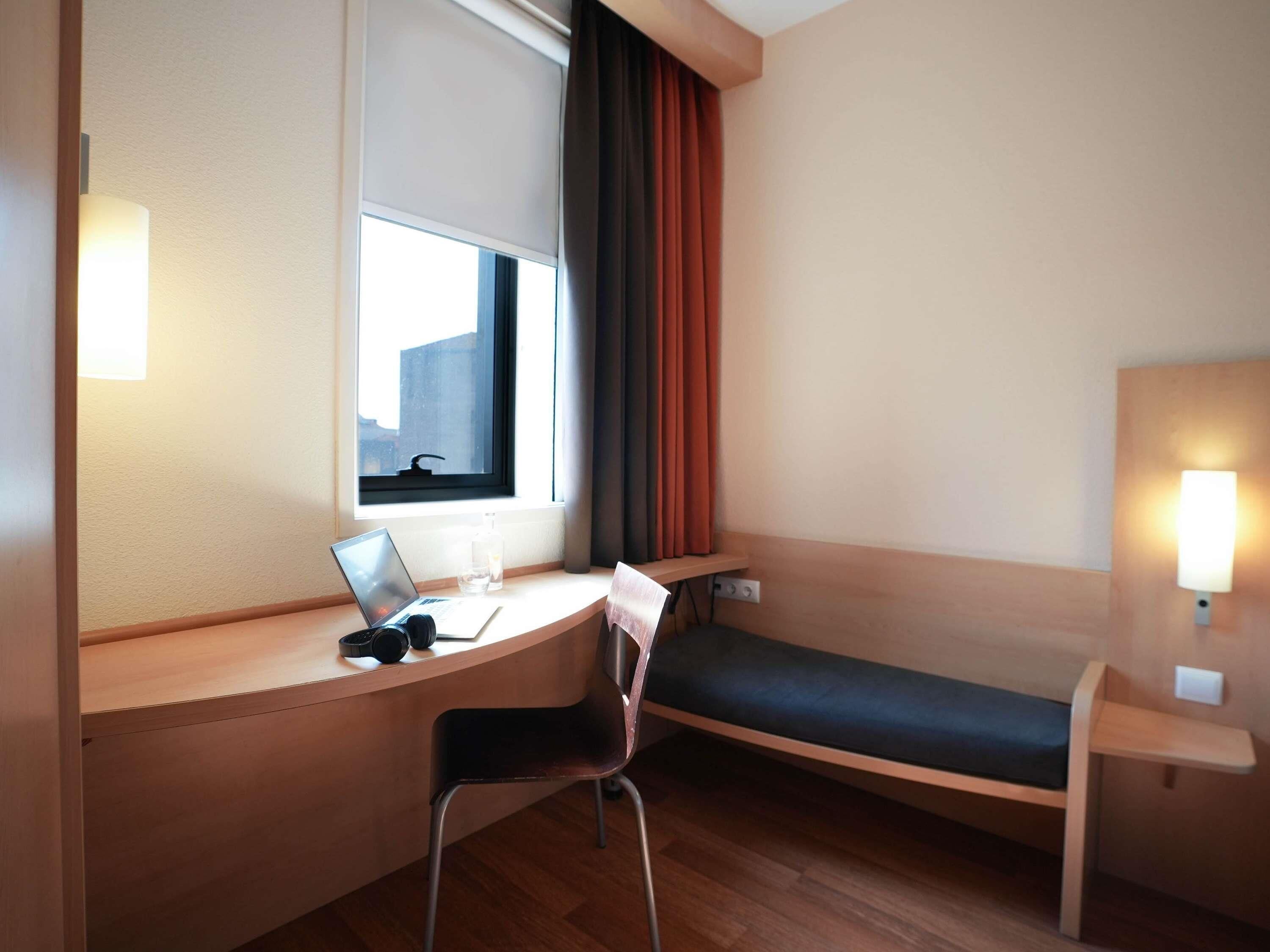 Une petite chambre d’hôtel avec un bureau, une chaise et un lit.