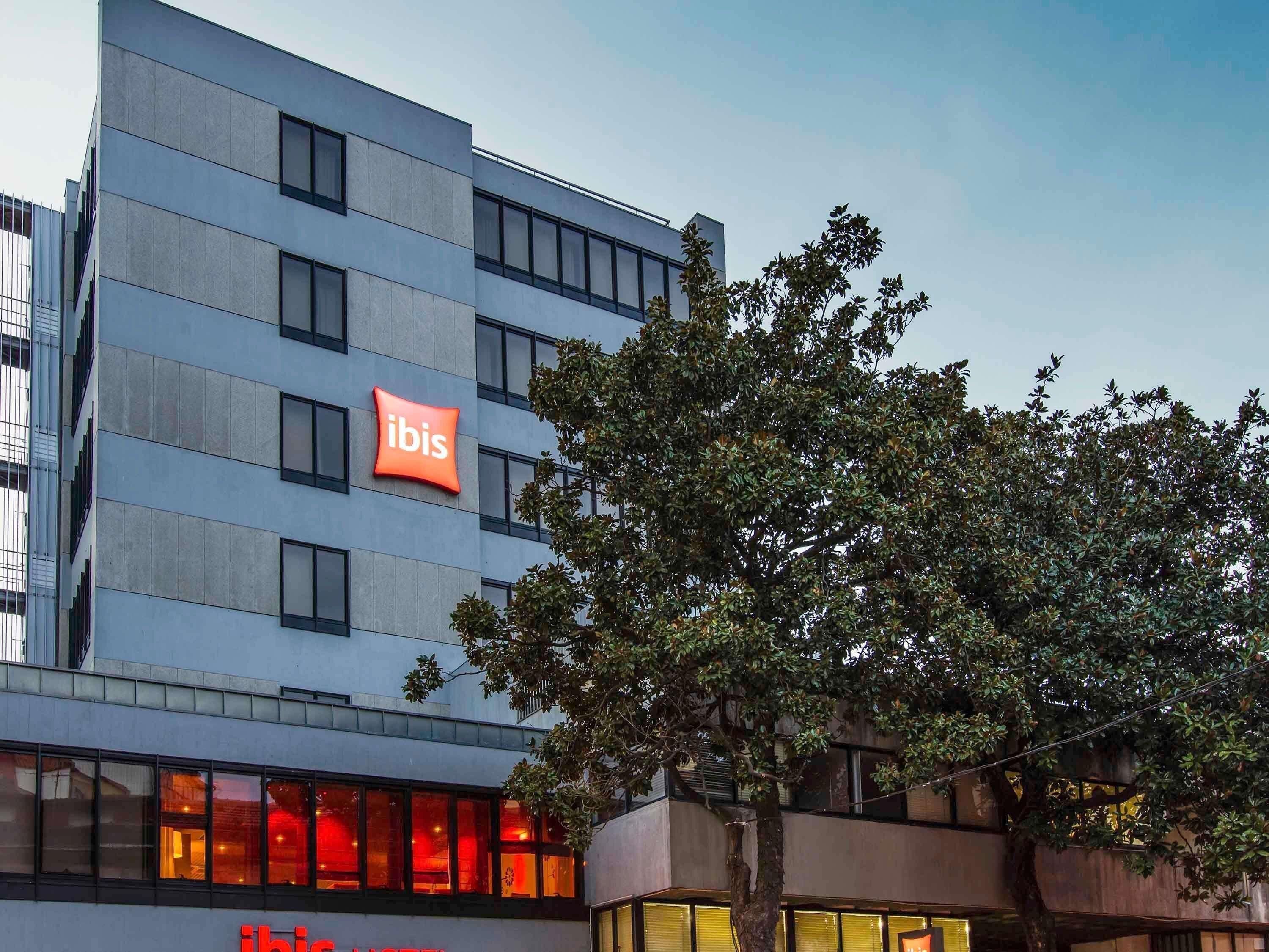 En moderne bygning med et tydeligt 'ibis' skilt, mange vinduer og et træ foran.