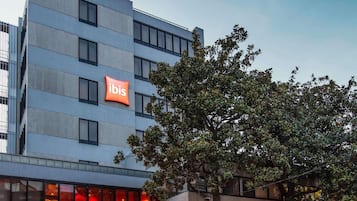 Un edificio moderno con un llamativo letrero de 'ibis', varias ventanas y un árbol frente a él.