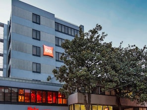 A modern building with a prominent 'ibis' sign, multiple windows, and a tree in front. - ibis Porto Centro São Bento (Porto)