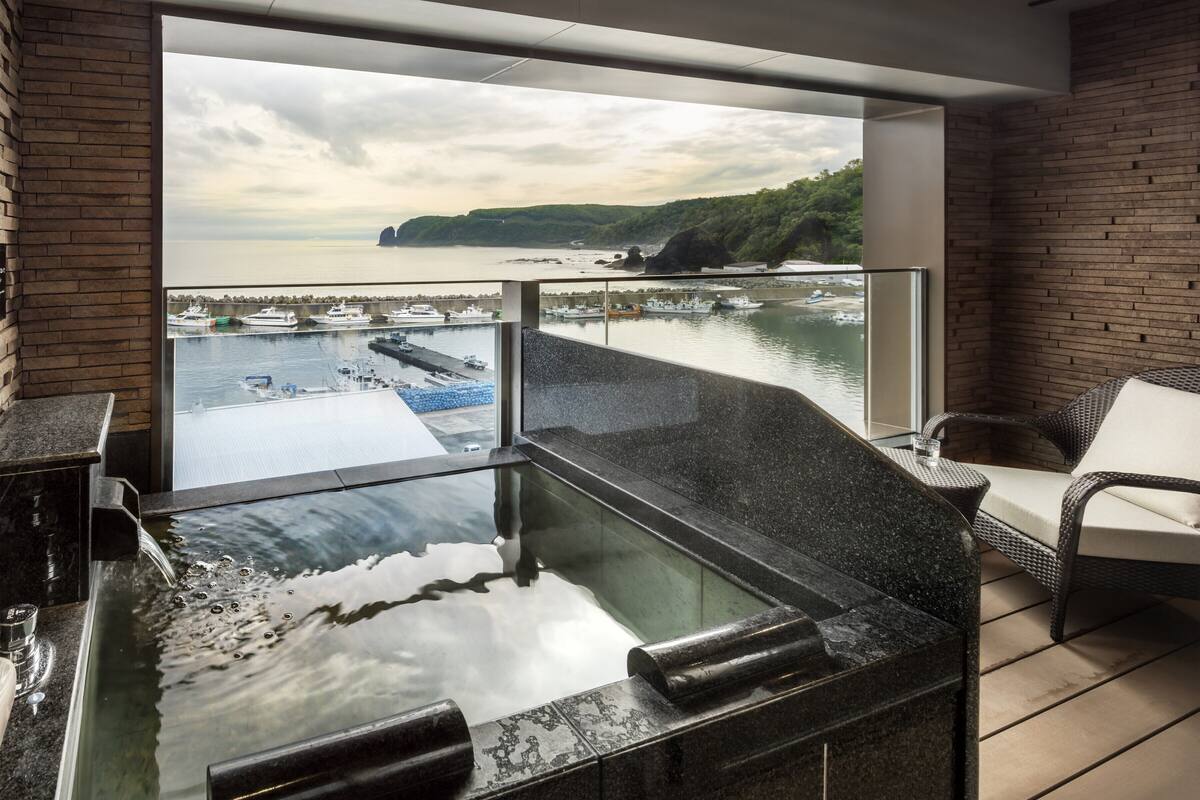 Un balcon avec un jacuzzi, une vue sur les bateaux et un port de plaisance, ainsi que des meubles en osier.