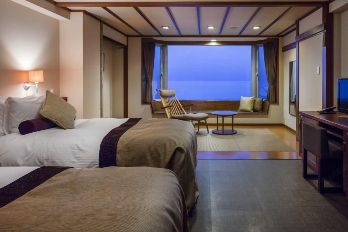 A hotel room with two beds, a small table, a chair, and a TV.