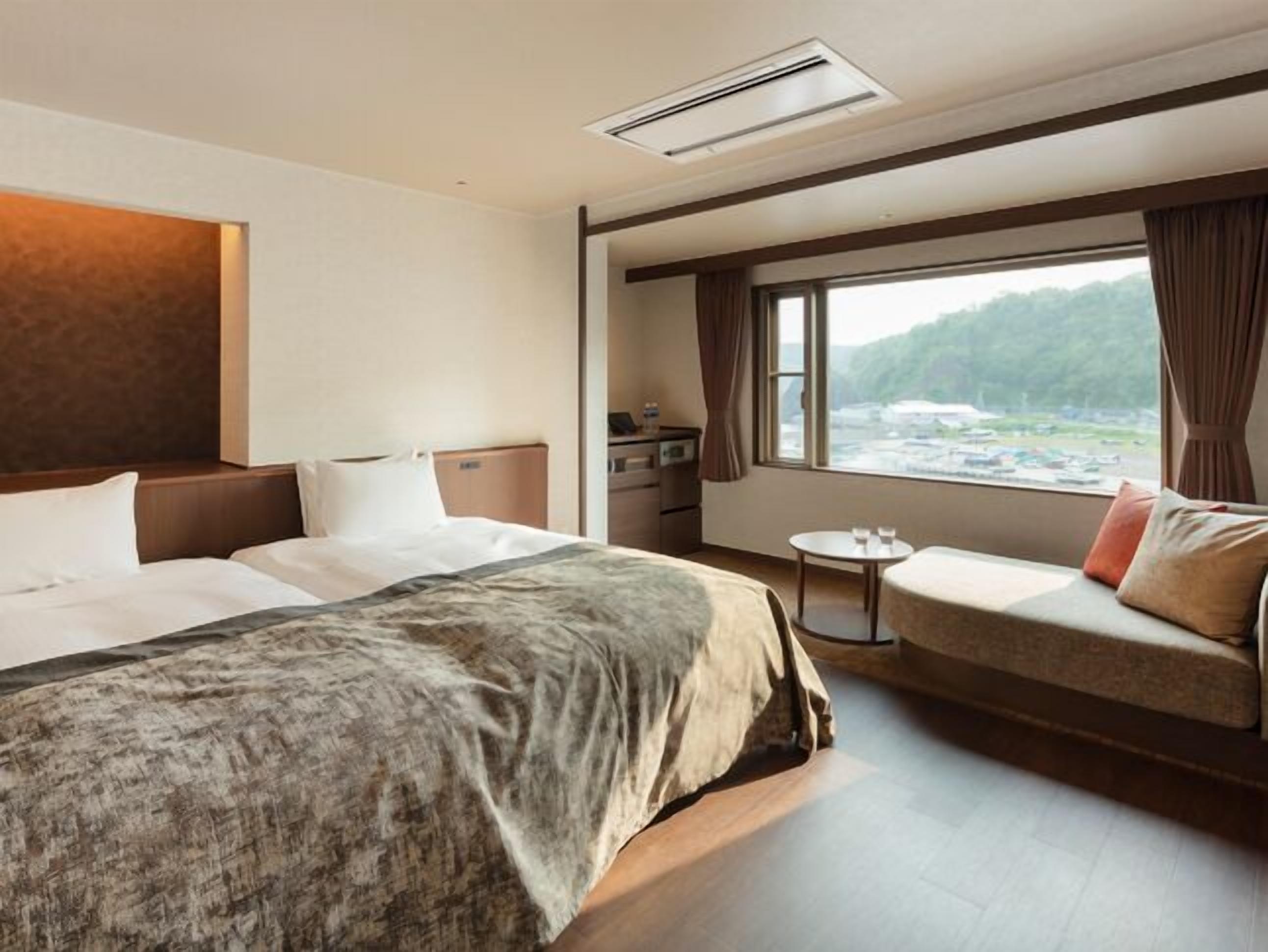 A hotel room with a large bed, a sofa, a small table, and a window with a view of the outdoors.