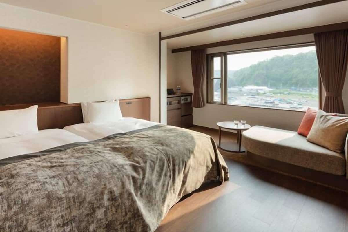 Habitación de hotel con una cama grande, un sofá, una mesita y un ventanal con vistas al exterior.