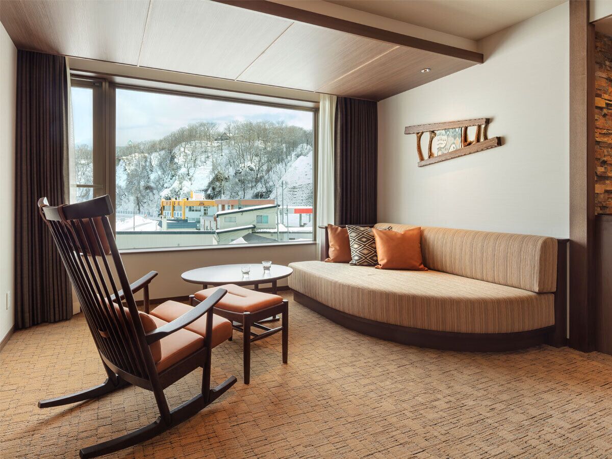 Una habitación de hotel con un ventanal grande, un sofá, una silla de madera y una pequeña mesa.