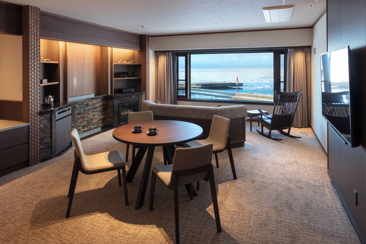 Une chambre d’hôtel moderne dotée d’un coin repas, d’un canapé, d’une télévision et offrant une vue sur l’océan.