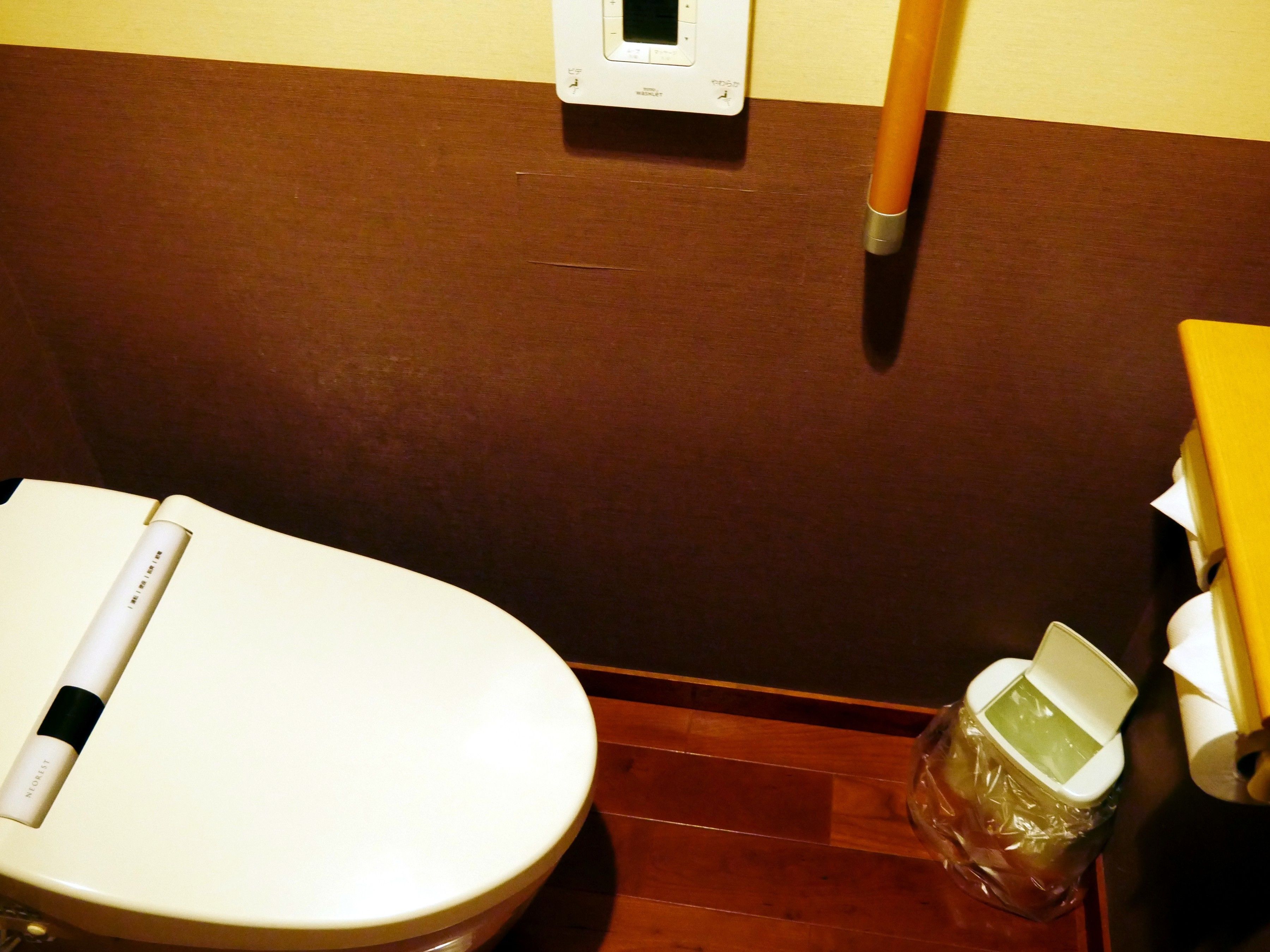 A bathroom with a toilet, a hand sanitizer dispenser, and a trash bin.