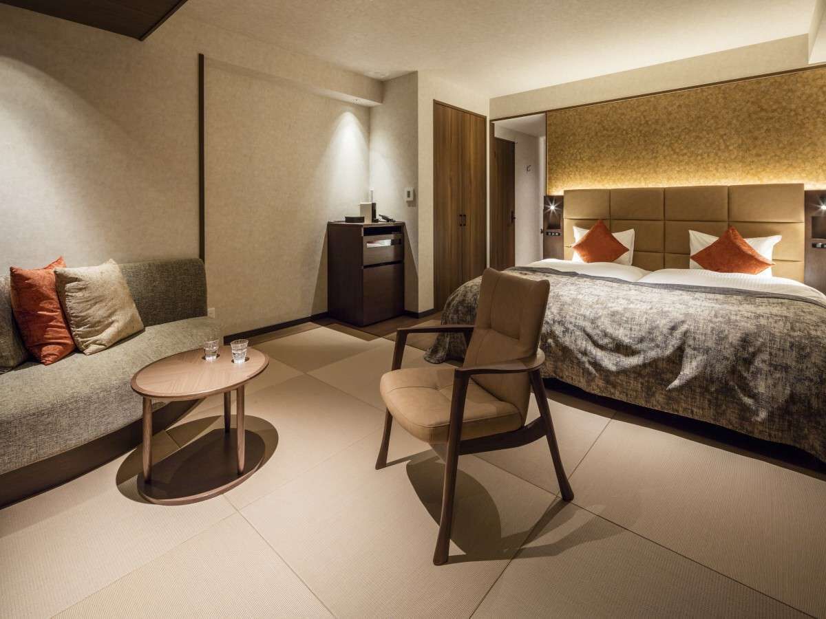 A modern hotel room with a bed, a sofa, a chair, and a small table.