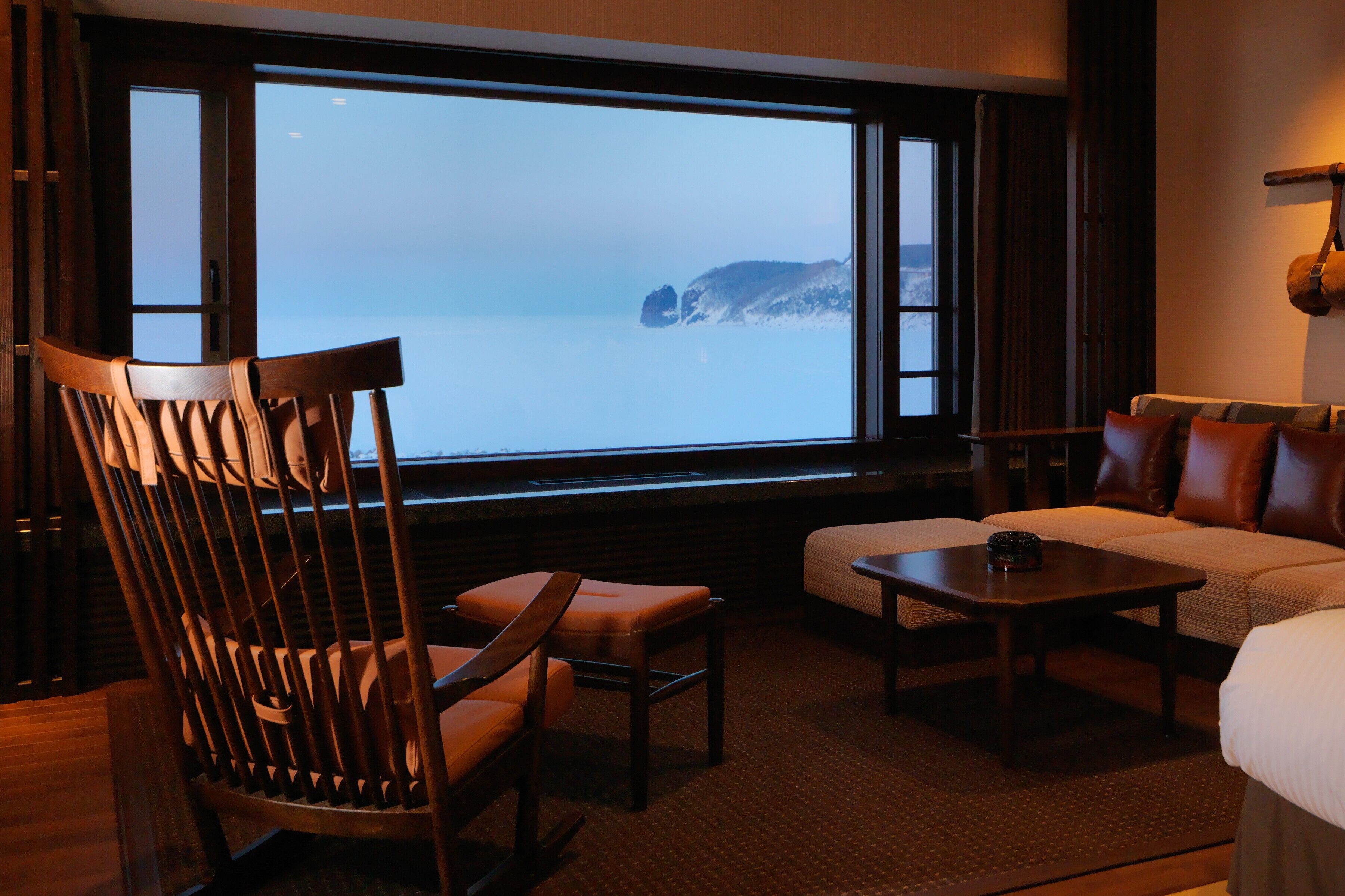 A room with a large window, a wooden chair, a sofa, and a small table.