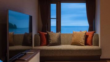 Una sala de estar moderna con un televisor de pantalla plana grande, un sofá con muchos cojines y vistas al océano a través de amplias ventanas.