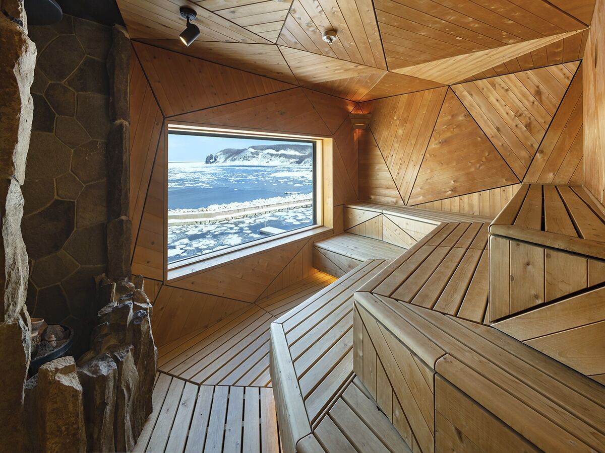 A wooden sauna with a stone wall and a window offering a view of a snowy landscape.