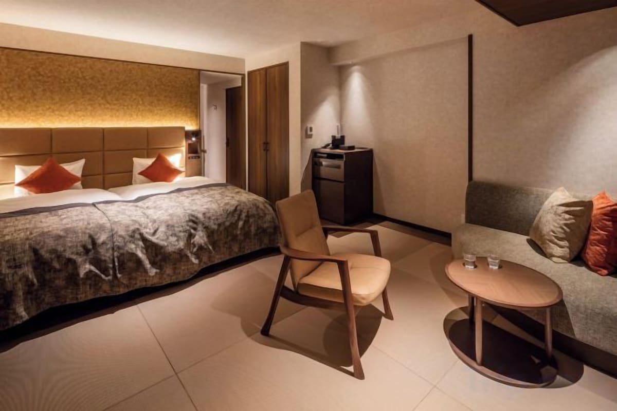 A modern hotel room with a bed, a sofa, a chair, and a small table.