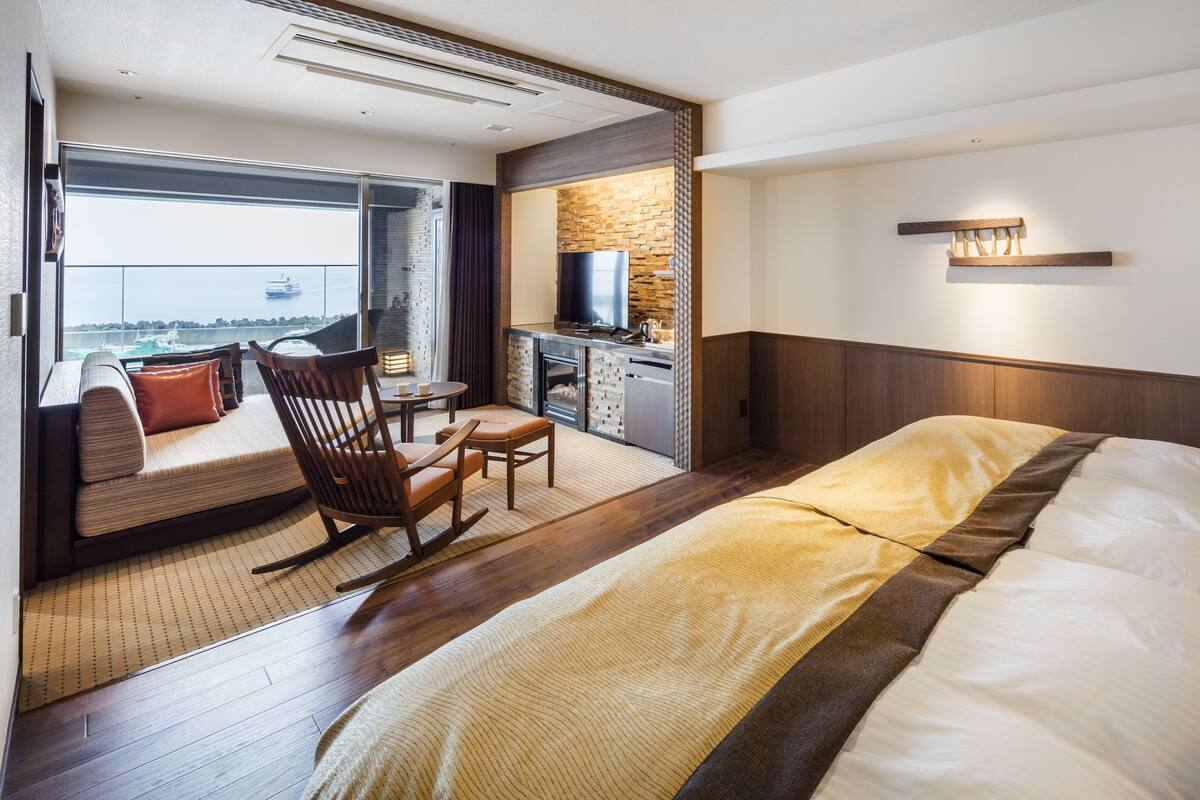 Une chambre d’hôtel dotée d’un grand lit, d’un coin salon avec vue sur la mer, d’une petite kitchenette et d’un téléviseur.