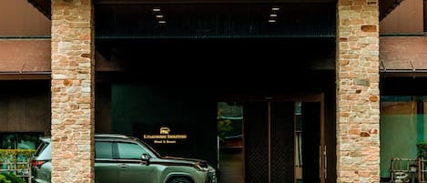 A building entrance with stone pillars, a parked SUV, and a sign for Kitakubushi Shiretoko Hotel & Resort.
