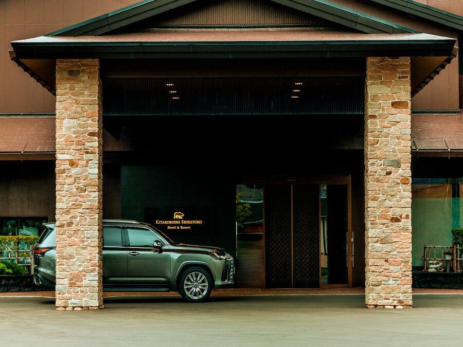 A building entrance with stone pillars, a parked SUV, and a sign for Kitakubushi Shiretoko Hotel & Resort.