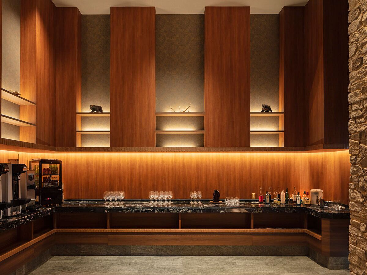 A modern bar area with wooden paneling, a marble countertop, and shelves with bottles and glasses.