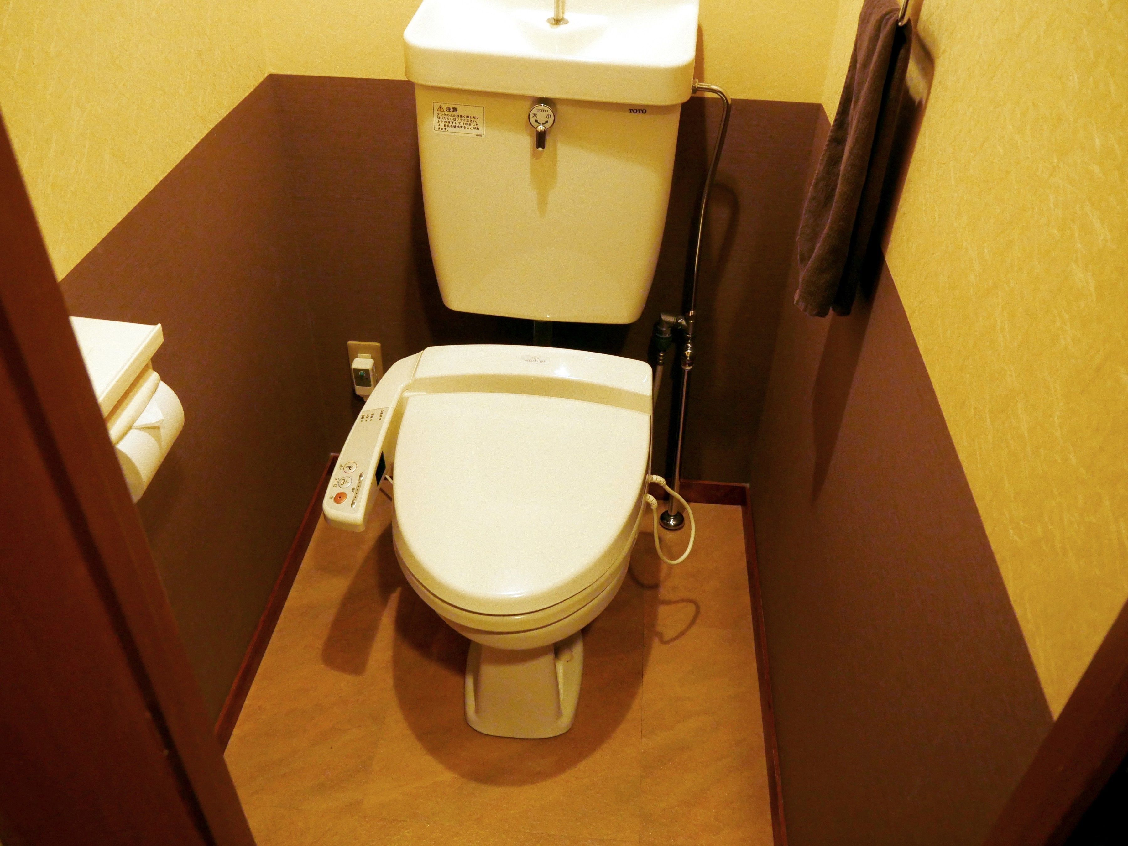 Un WC compatto con un pannello di controllo, un serbatoio dell'acqua a vista e un asciugamano su un porta asciugamani.