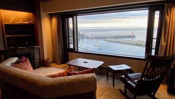 Ein gemütliches Zimmer mit einem großen Fenster und Blick auf einen Hafen, einem kleinen Tisch, einem Stuhl und einem Sofa.