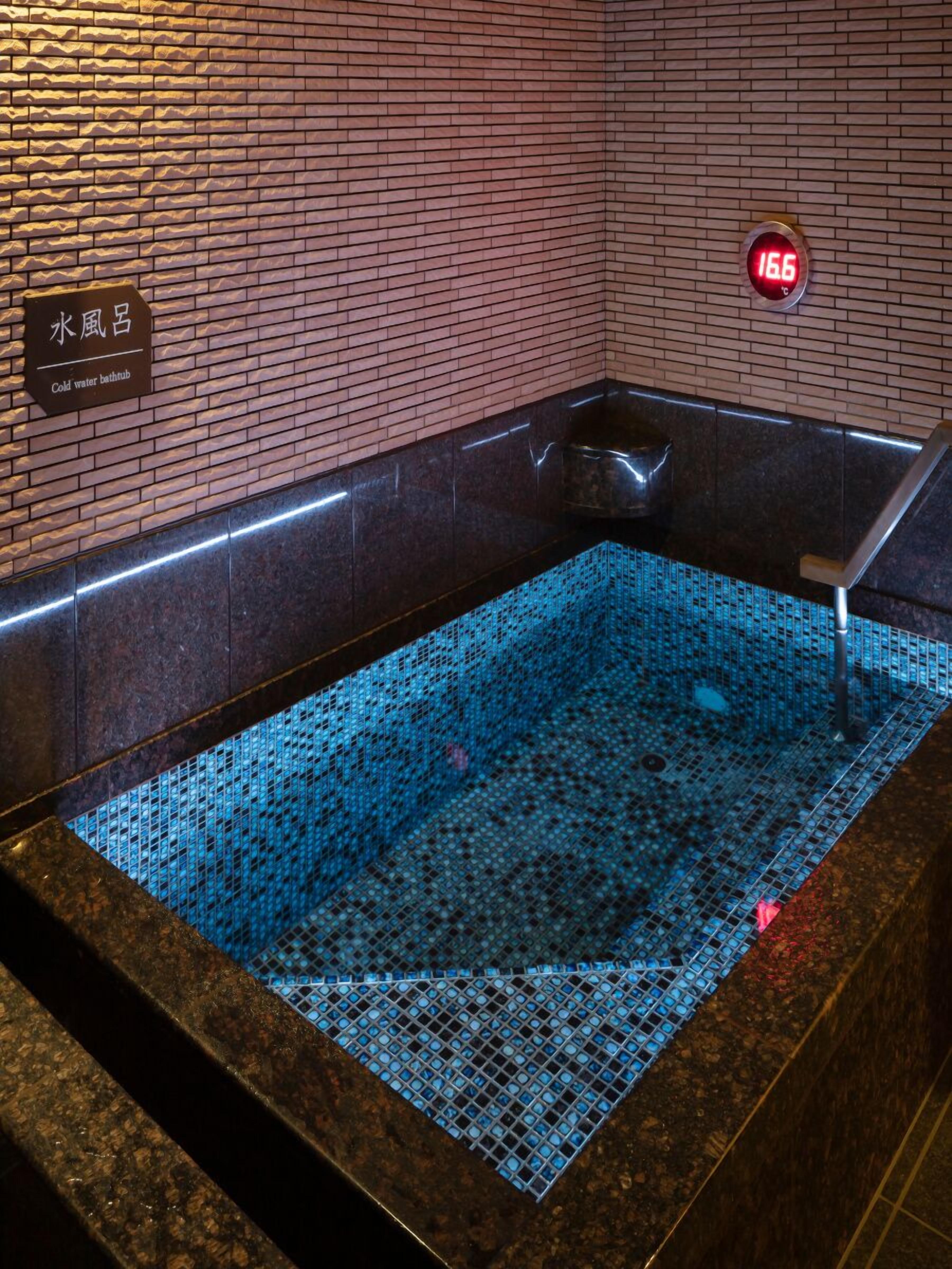 Zona de spa con suelo de mosaico azul, indicador de temperatura y cartel que señala una bañera de hidromasaje con agua fría.