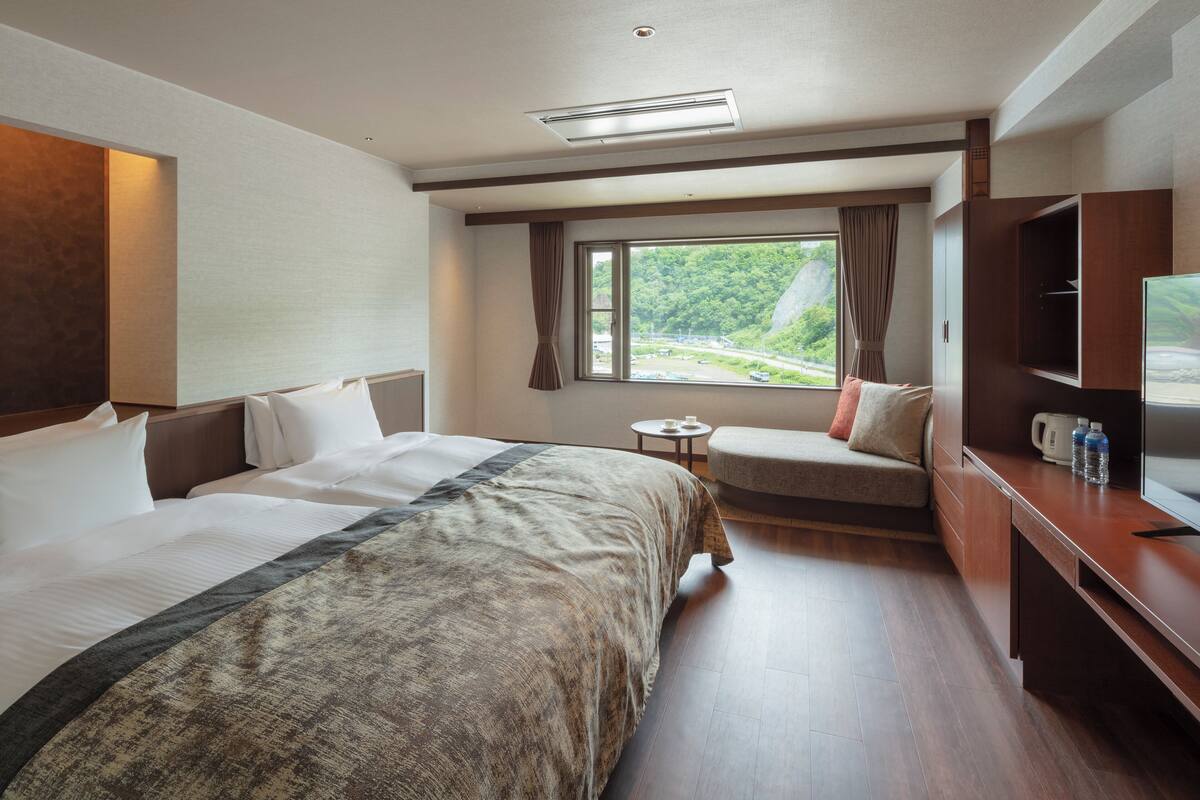 Une chambre d’hôtel avec un grand lit, un canapé, une télévision et une fenêtre donnant sur un paysage verdoyant.