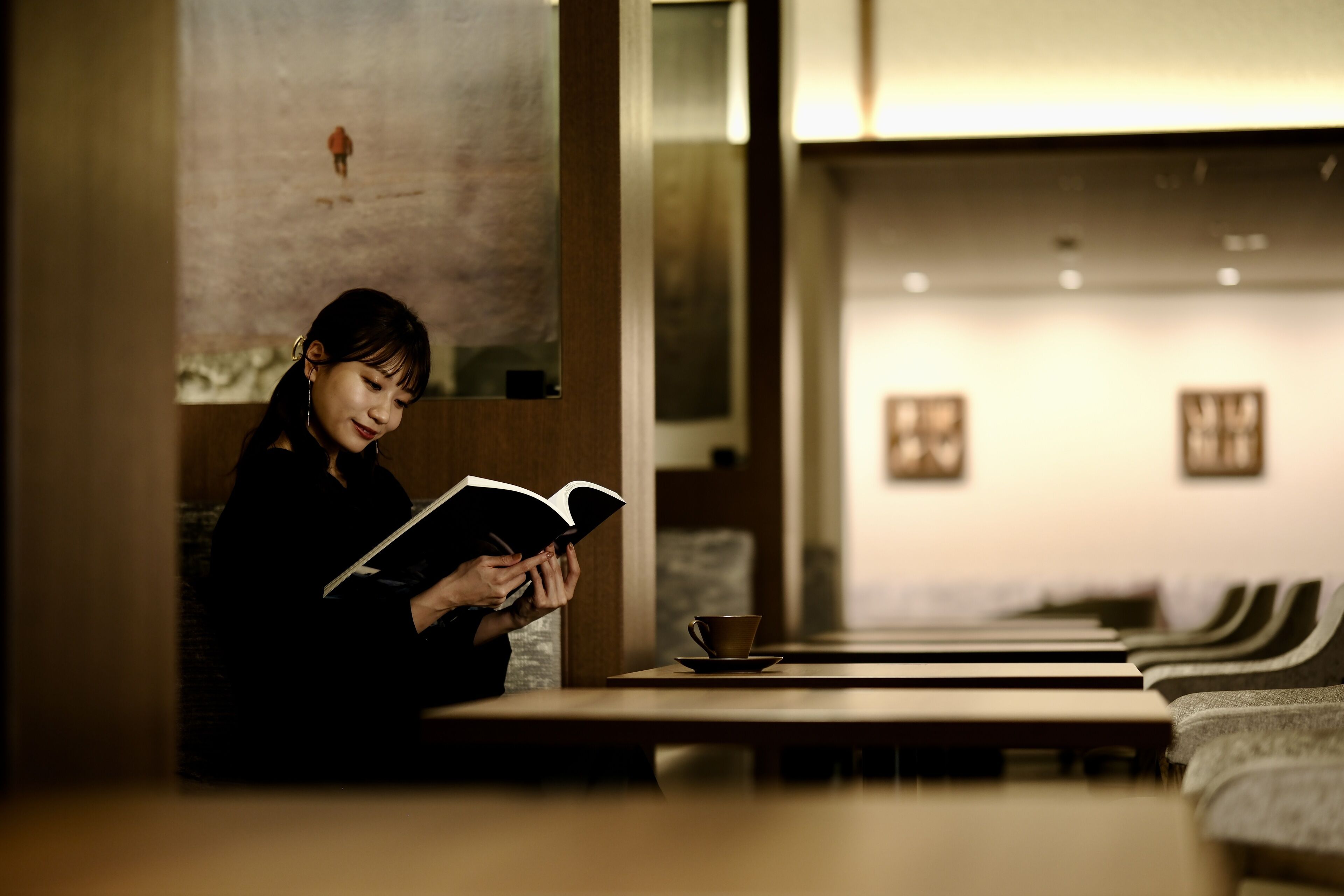 A person reading a book at a table in a cafe with a modern interior and a row of empty chairs.