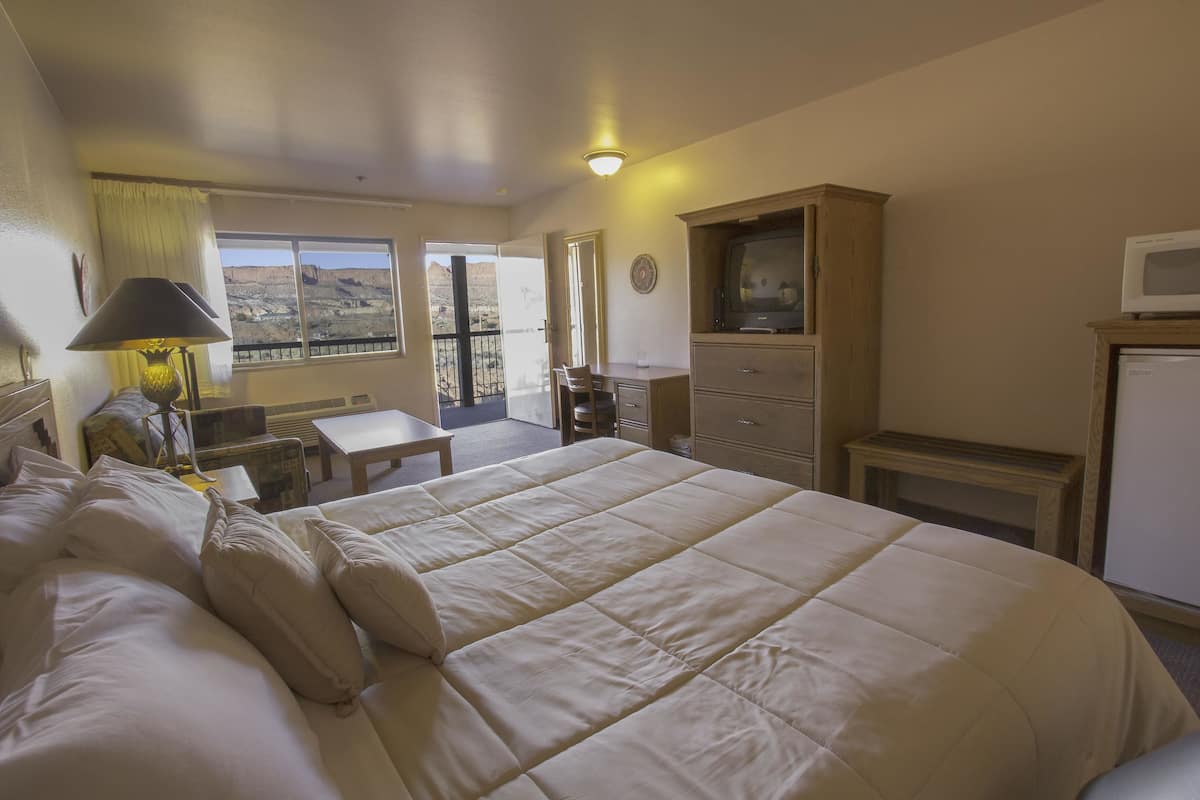 Ein Hotelzimmer mit einem großen Bett, einem Schreibtisch, einem Fernseher und Blick auf die Berge.