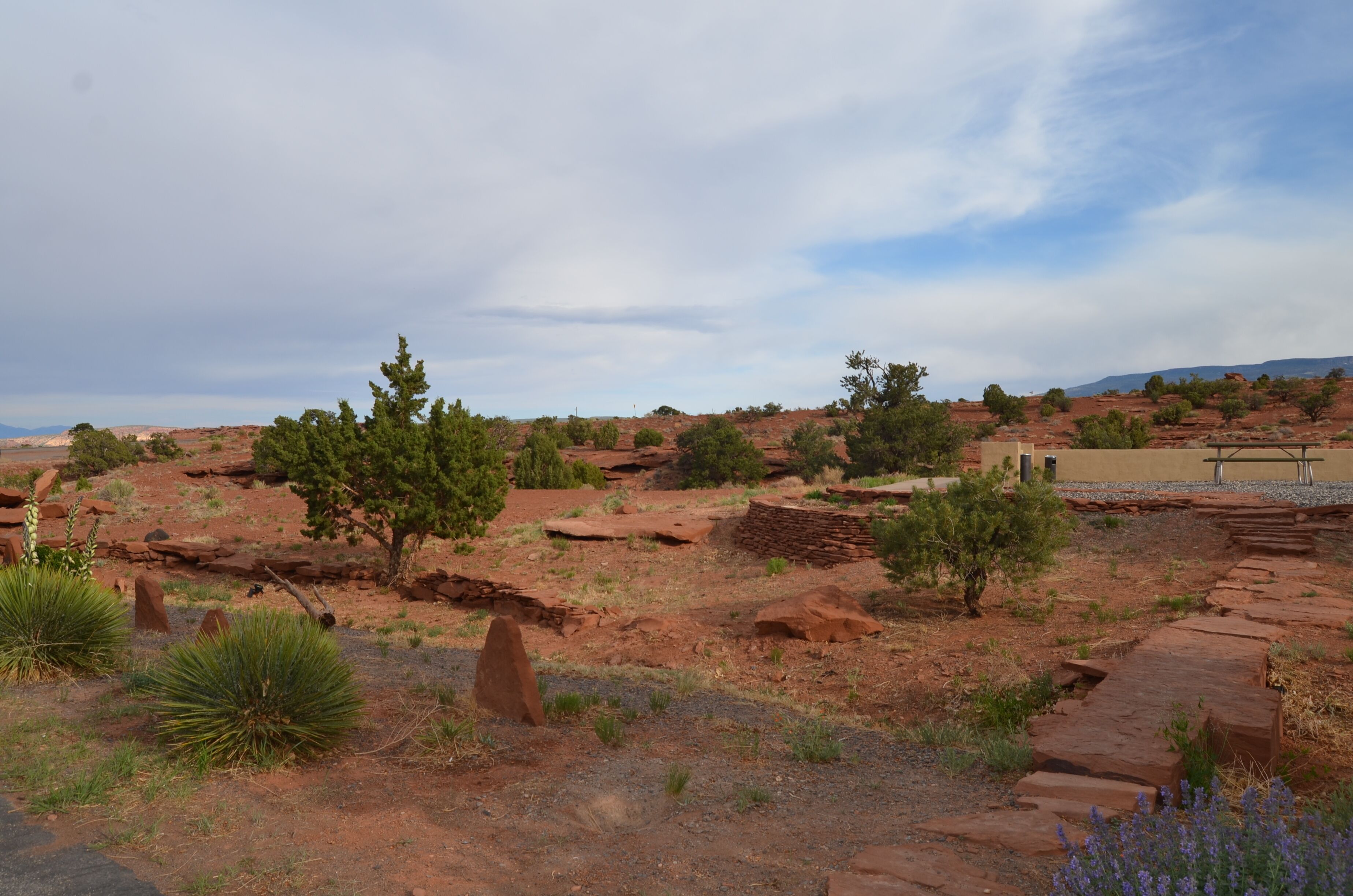A desert landscape with sparse vegetation, a stone structure, and a clear sky.