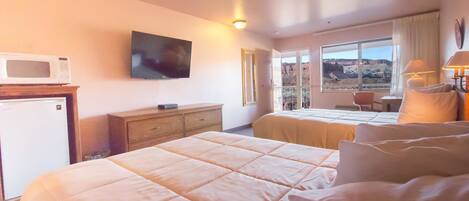 Habitación de hotel con cama, televisor montado en la pared, escritorio con silla y ventana con vistas a las montañas.