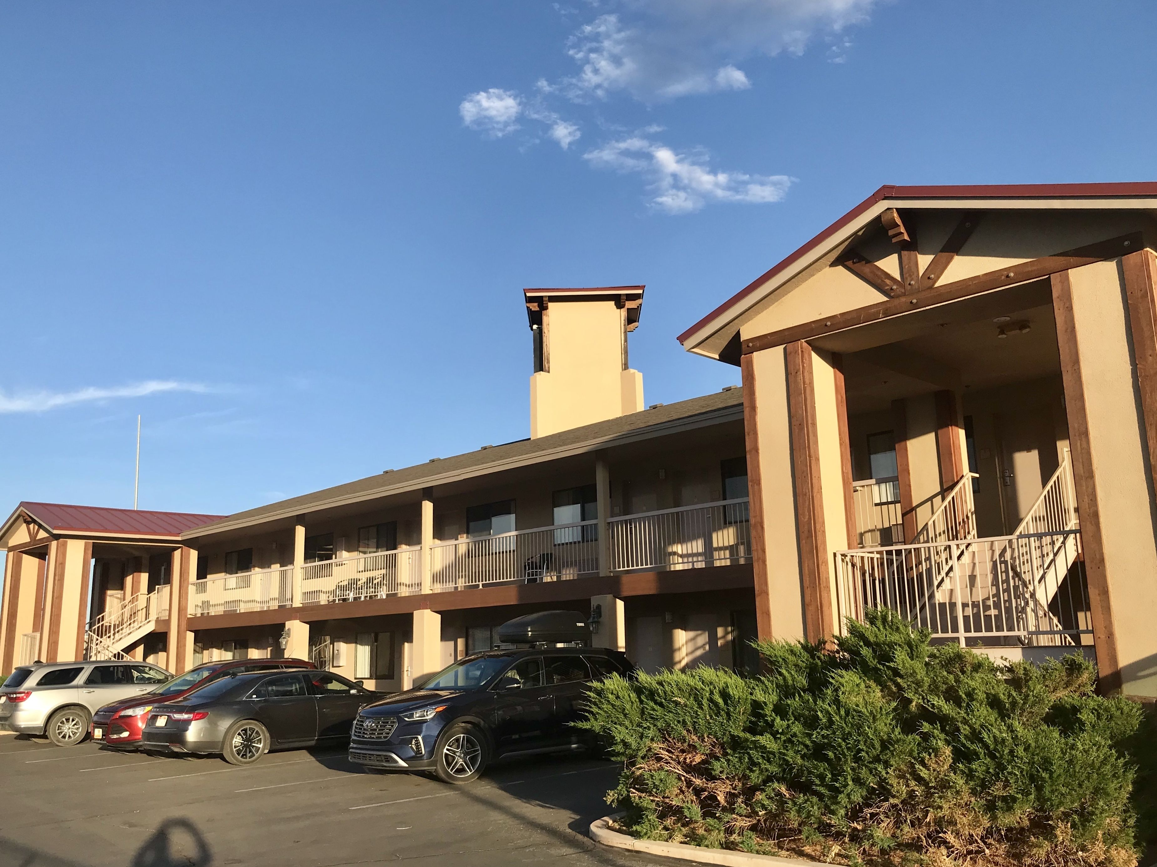 A multi-story motel with a parking lot, outdoor seating, and a staircase leading to the upper floors.