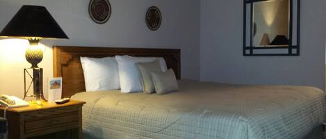 A neatly made bed with a quilted cover, a bedside lamp, a nightstand with a telephone, and two wall-mounted decorative plates.