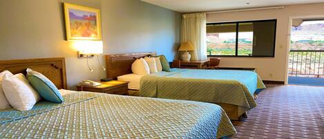 Habitación de hotel con dos camas, una mesita de noche con lámpara, un cuadro en la pared y una ventana con vistas al exterior.