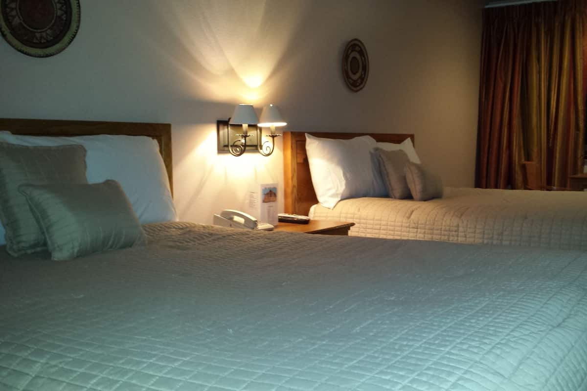 Ein Hotelzimmer mit zwei Betten, einem Nachttisch, einer Lampe, einem Telefon und einem Fenster mit Vorhängen.