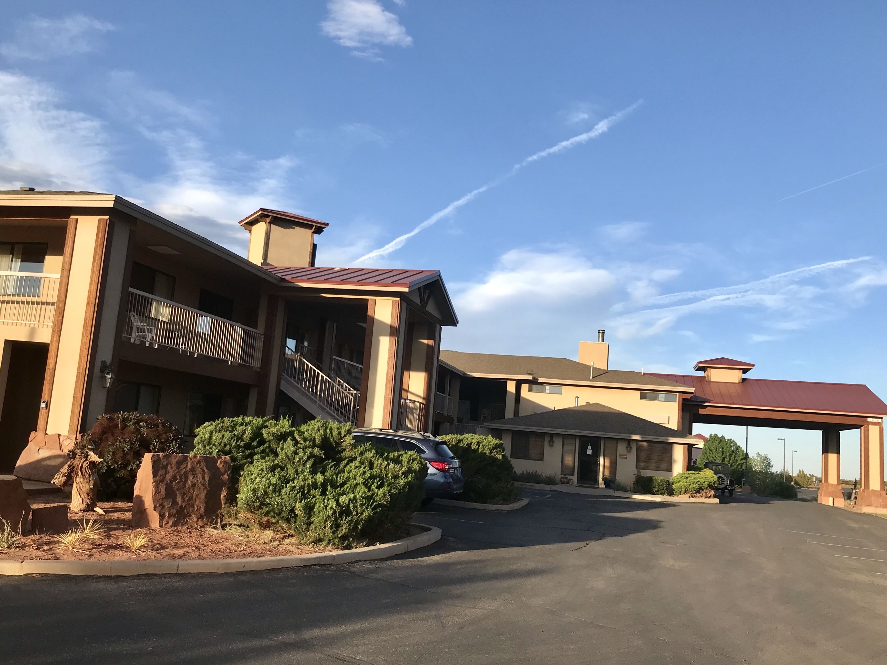 A hotel with a covered outdoor area, a parking lot, and a clear sky.