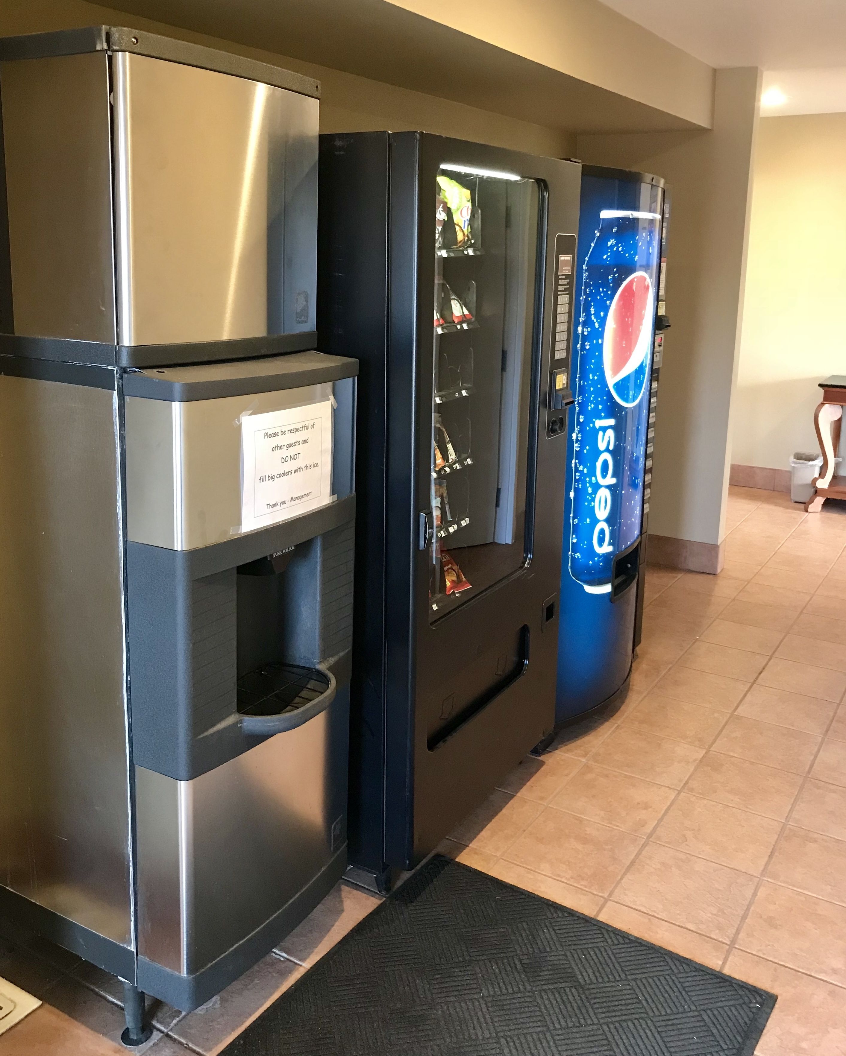 A vending machine with a Pepsi logo, a stainless steel refrigerator, and a sign requesting guests to be respectful and not to fill big bottles with the machine.