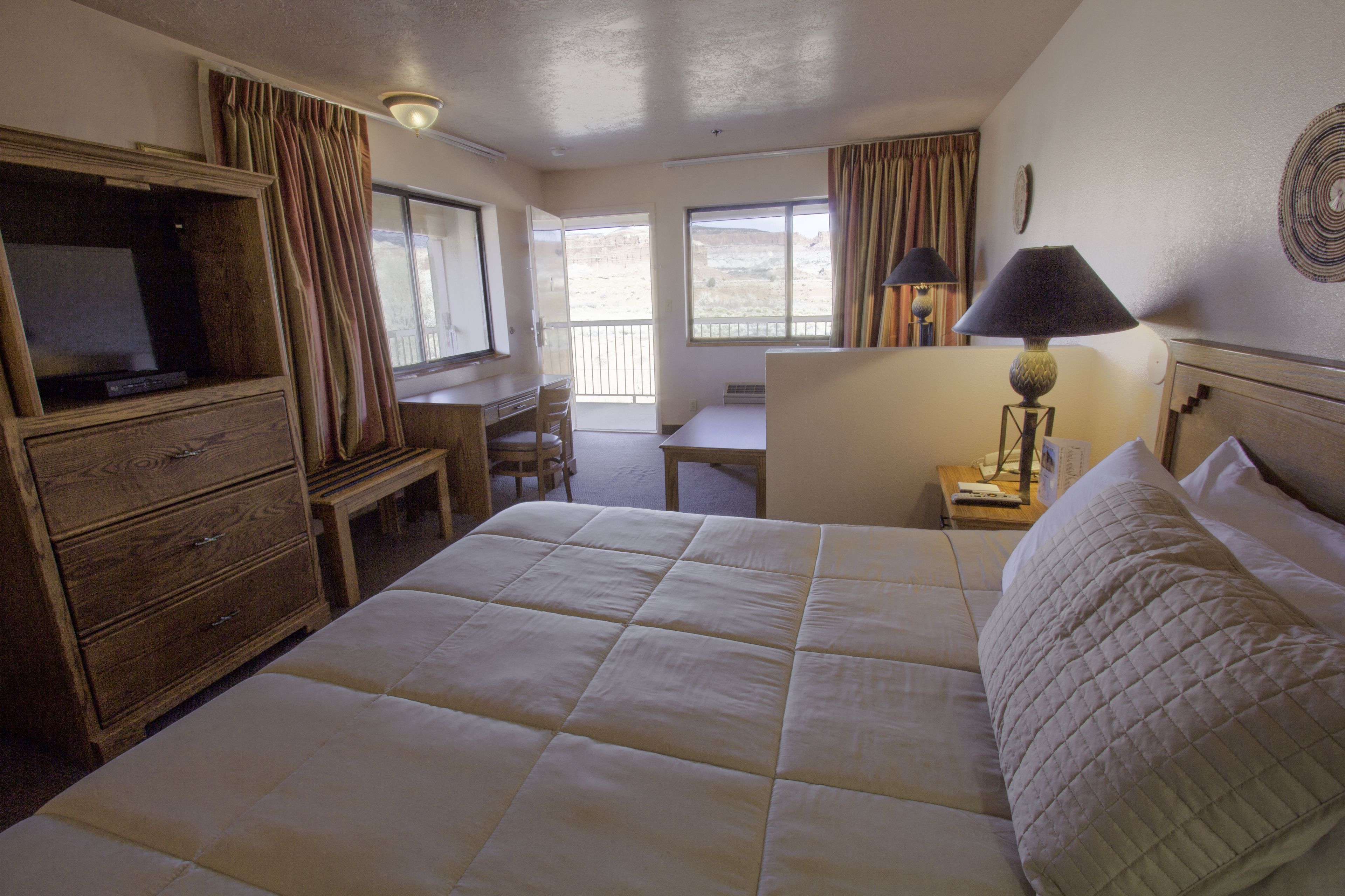 A hotel room with a large bed, a desk, a chair, a television, and a lamp.