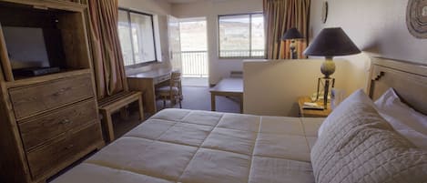 A hotel room with a large bed, a desk, a chair, a television, and a lamp.