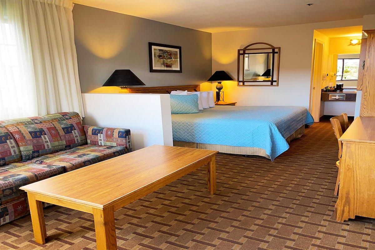 Ein Hotelzimmer mit einer Couch, einem Bett mit blauer Bettdecke, einem Holztisch, einer Lampe und einem Spiegel.