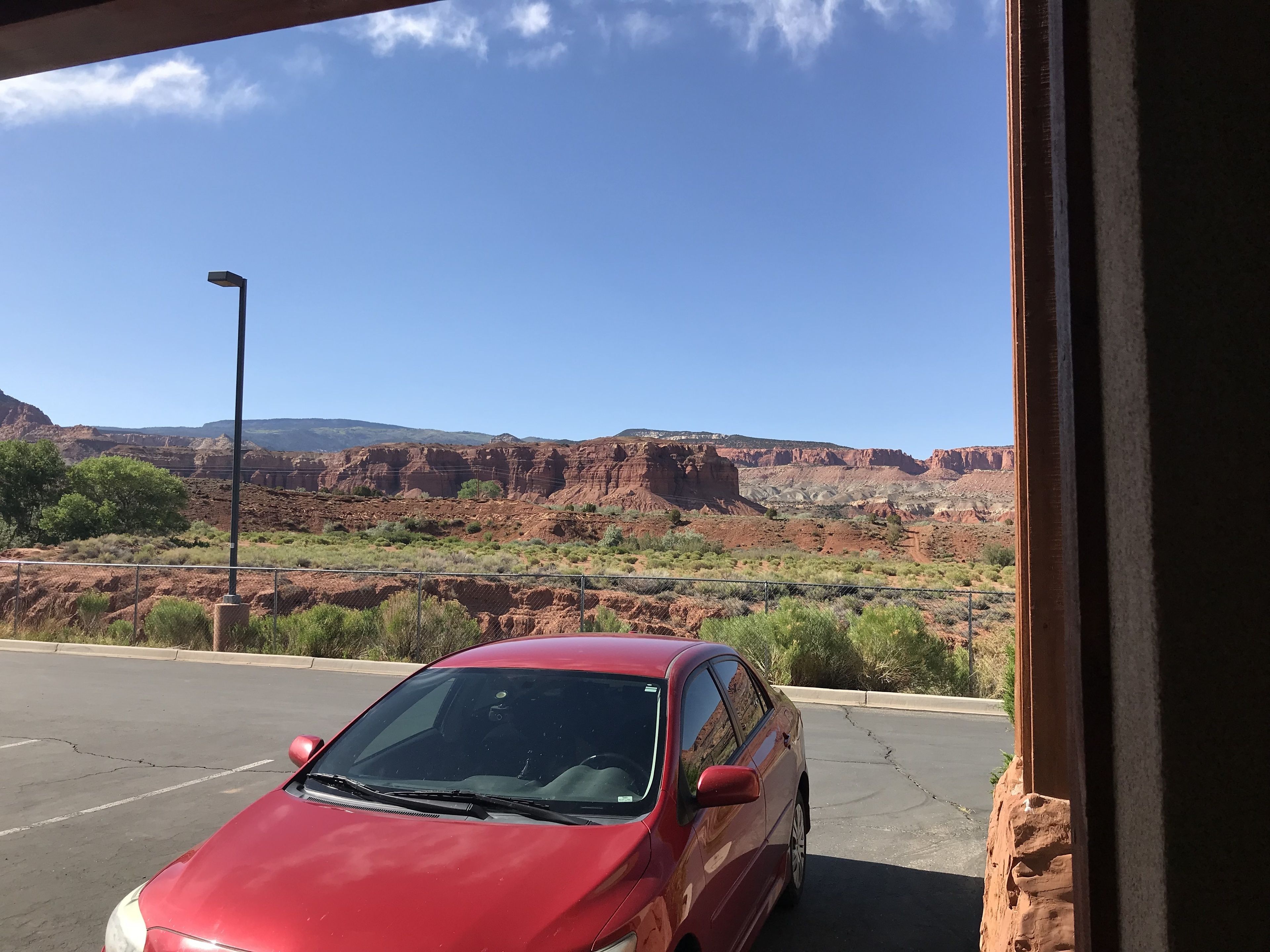 Ein rotes Auto geparkt in einer Wüstenlandschaft mit roten Felsformationen im Hintergrund.