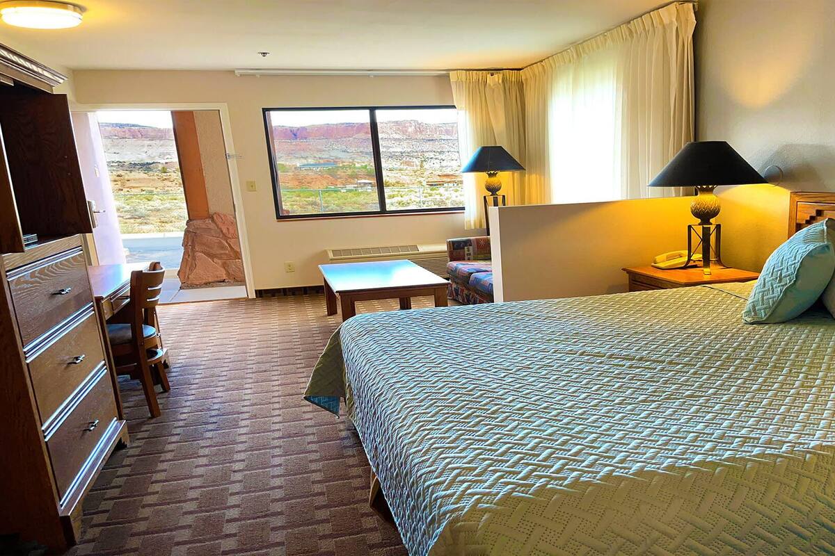 Ein Hotelzimmer mit einem großen Bett, einem Schreibtisch, einem Stuhl und Blick auf eine gebirgige Landschaft.