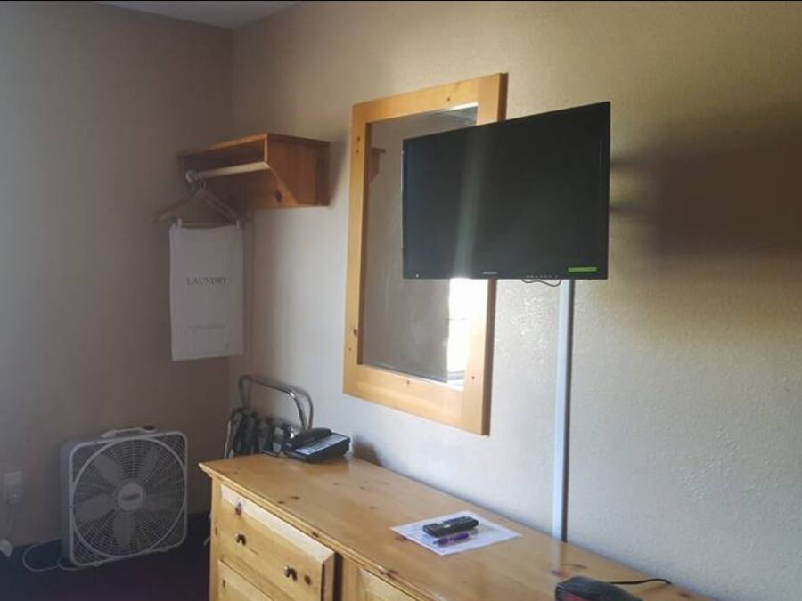 Una habitación pequeña con un aparador de madera, un escritorio, un espejo, un televisor y un ventilador.